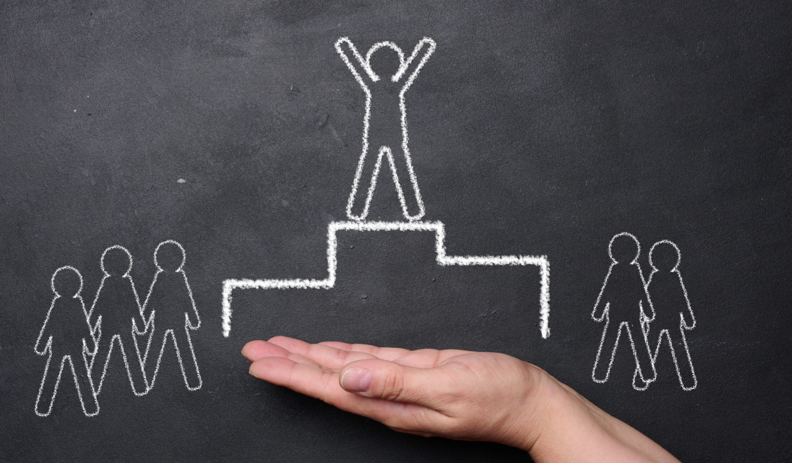 Hand holding a chalk drawing of a podium with a person on top an